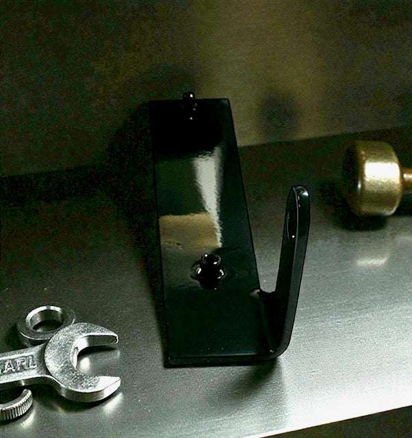Black metal hook with tools on a metallic surface, used for organizing or hanging items.